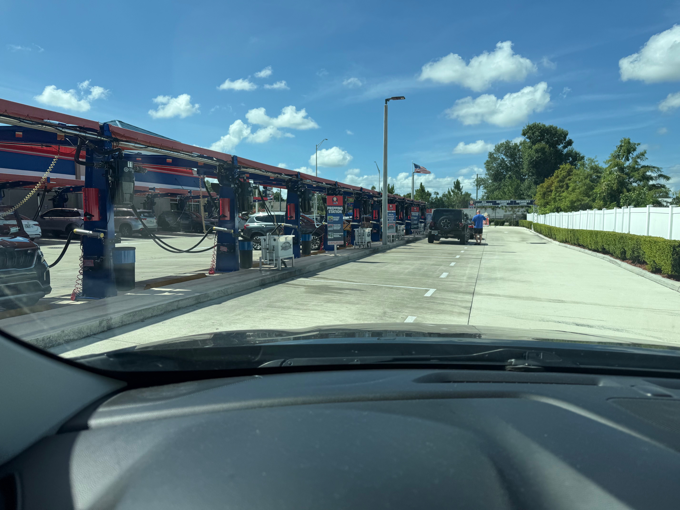 Big Dan's Car Wash on SR-64 in Bradenton, Florida — a row of covered self-serve prep stations with red-and-blue canopies, the Members Lane sign, and an American flag against a blue sky