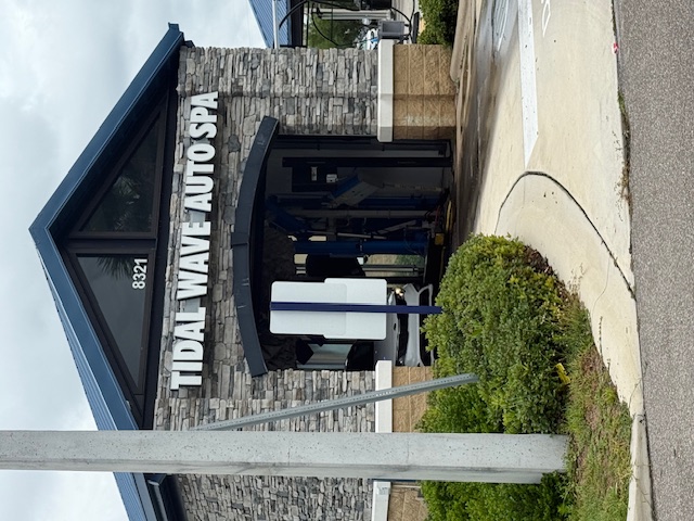 Tidal Wave Auto Spa entrance at 8321 FL-64 in Bradenton, Florida — a stone-veneer facade with a black metal gabled roof and the Tidal Wave Auto Spa sign above the tunnel arch