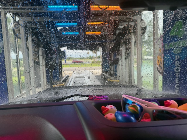 Inside the Tidal Wave Auto Spa tunnel during a wash — colorful blue and orange LED arches above the conveyor with foam and water visible on the windshield