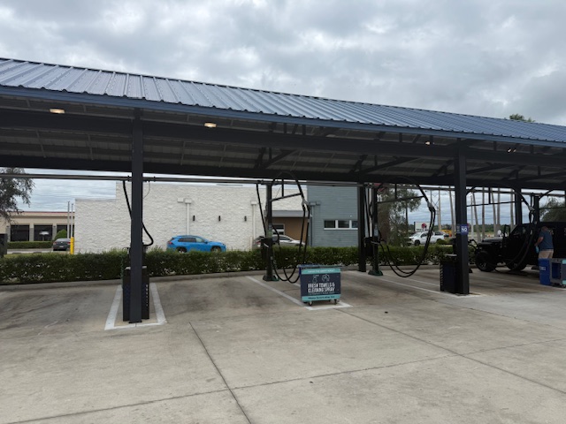 Covered free-vacuum bays at Tidal Wave Auto Spa Bradenton — multiple vacuum stations under a pitched metal canopy with the Fresh Towels and Cleaning Spray cart visible at the entrance